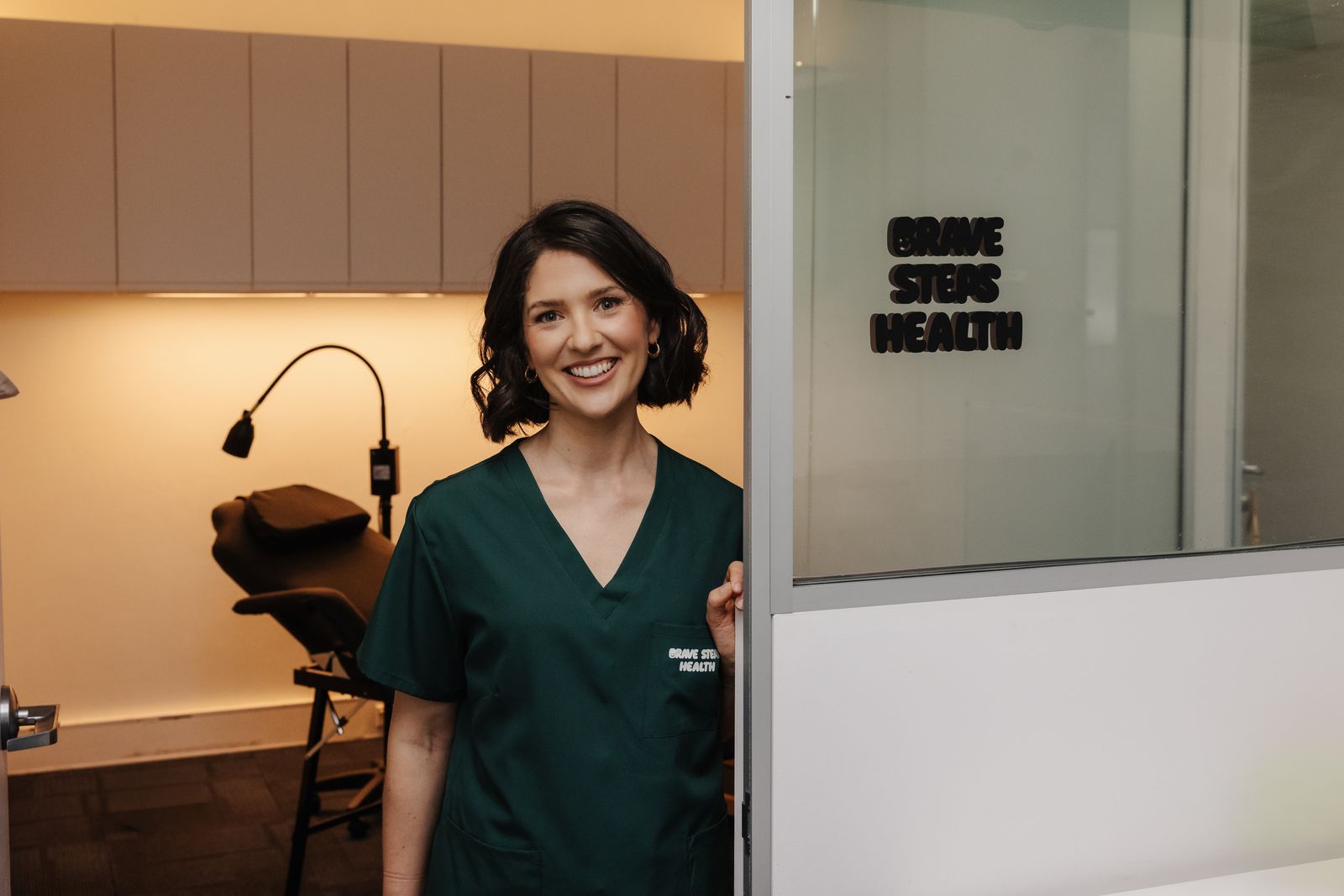Renee Collins, founder of Brave Steps Health, smiling in green scrubs at the door of the Brave Steps Health clinic in Gladesville, Sydney